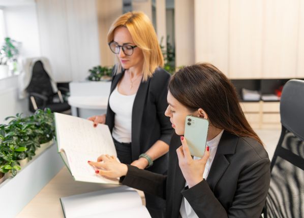 2 femmes derrières un bureau, en situation de travail et d'échange dont l'une est au tel.