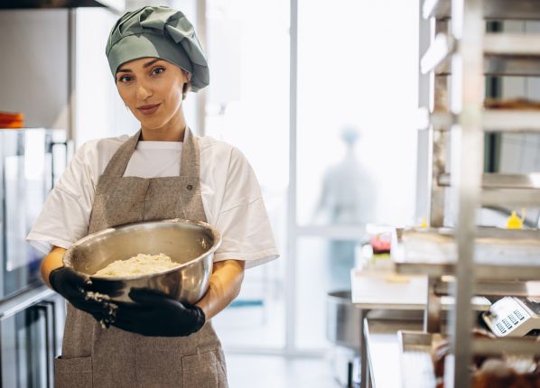 Une cuisinière de restauration collective en train de préparer un plat dans une cuisine centrale