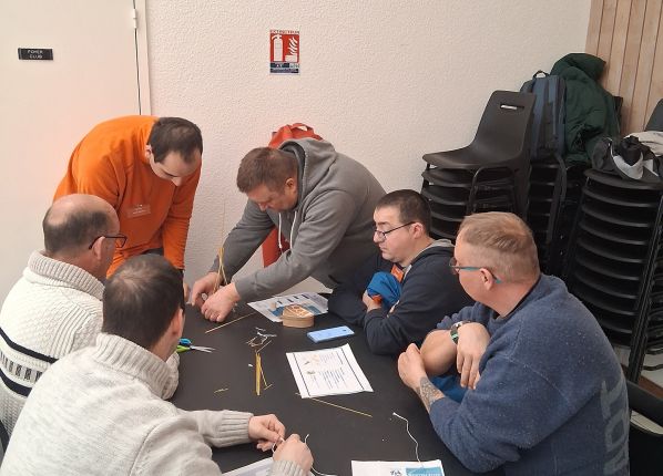Un groupe d'adultes en situation de handicap regardant un coordinateur de projet en train de leur expliquer une règle de travail dans un atelier
